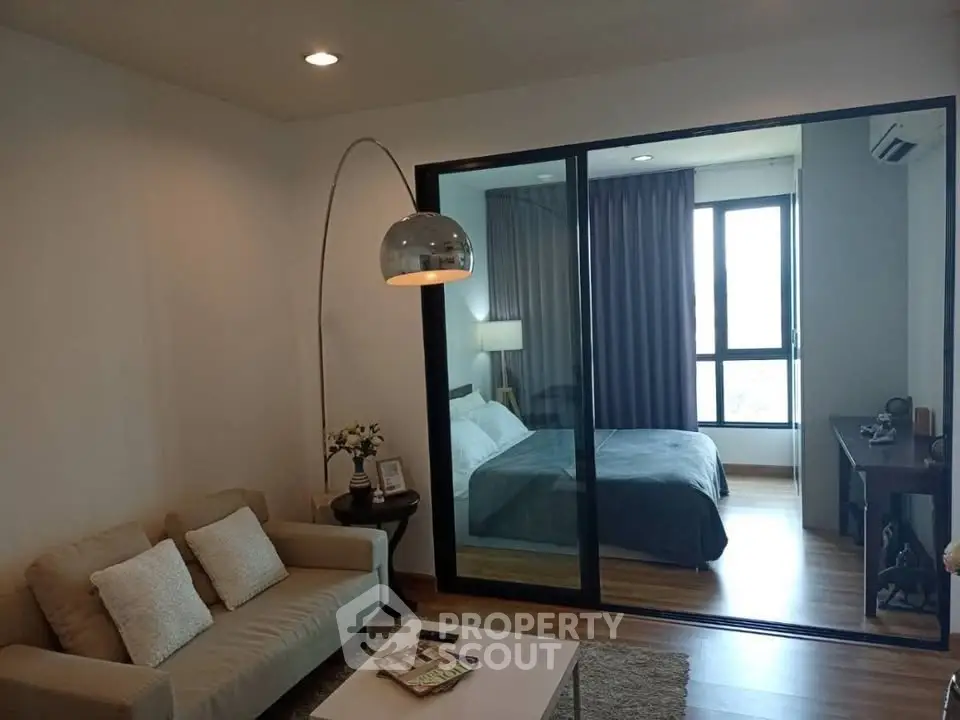 Modern living room with cozy sofa and stylish bedroom separated by glass partition.