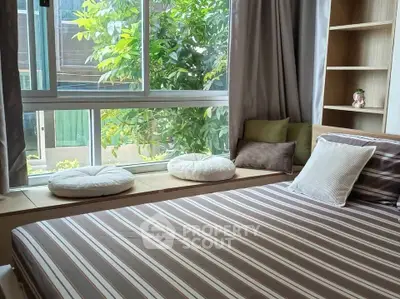 Cozy bedroom with large window and garden view, featuring stylish striped bedding and comfortable seating area.