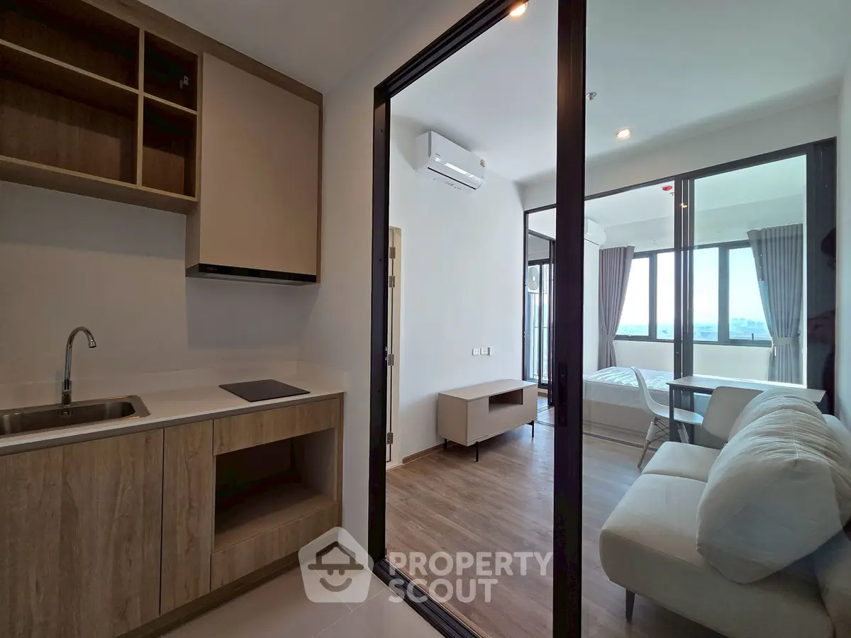 Modern apartment interior with open kitchen and cozy living area leading to a bright bedroom.
