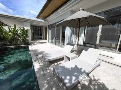 Luxurious poolside patio with modern sun loungers and umbrella in a serene villa setting.