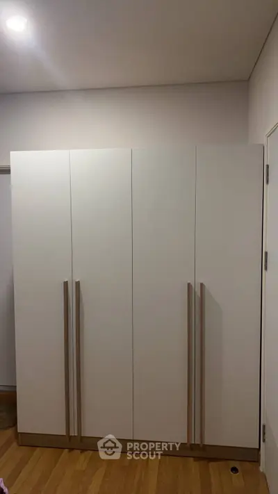 Modern white wardrobe with sleek handles in a minimalist room setting.