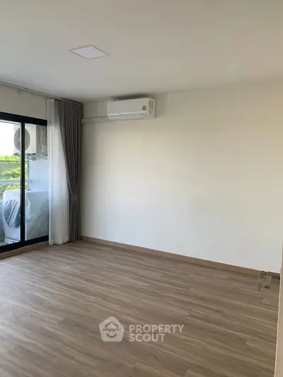 Spacious empty room with wooden flooring and large window for natural light.