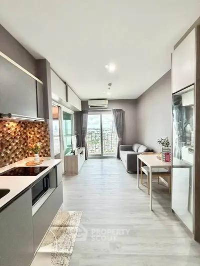 Modern open-plan living room with kitchen, featuring sleek design and large windows for natural light.