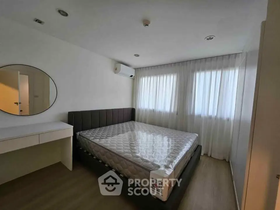 Modern bedroom with large bed, round mirror, and natural light from two windows.