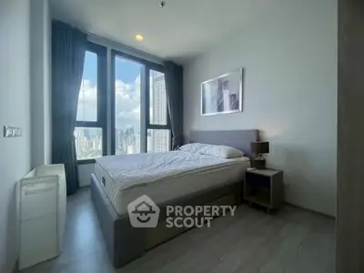 Modern bedroom with large windows offering stunning city views, featuring a comfortable bed and stylish decor.