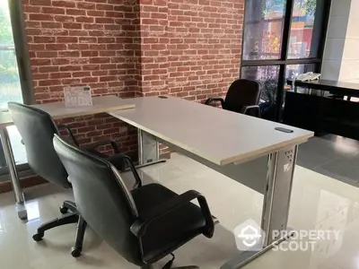 Modern office space with sleek desk and chairs, exposed brick wall, and large windows for natural light.