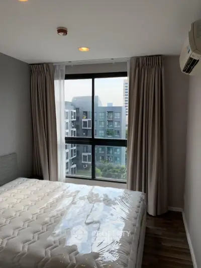Modern bedroom with large window offering city view, featuring a comfortable bed and elegant curtains.