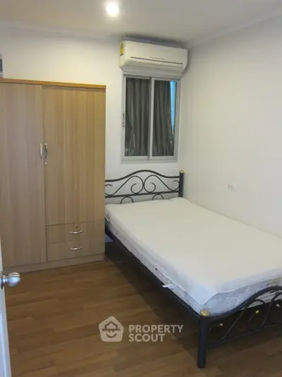 Cozy bedroom with wooden wardrobe and metal bed frame, featuring air conditioning and wooden flooring.
