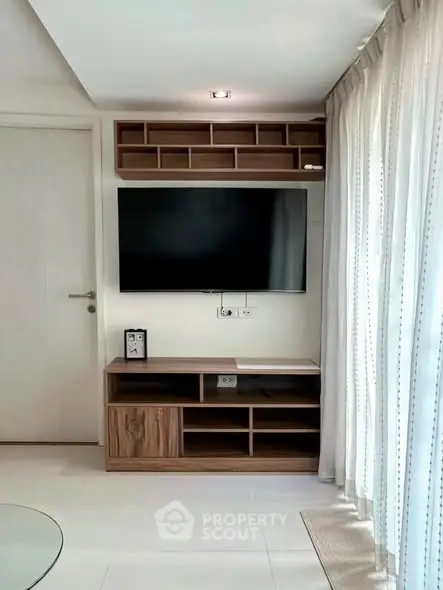 Modern living room with sleek TV unit and natural light from large windows.
