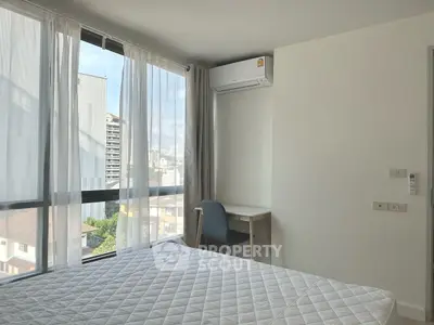Bright bedroom with large windows and city view, featuring a desk and air conditioning.
