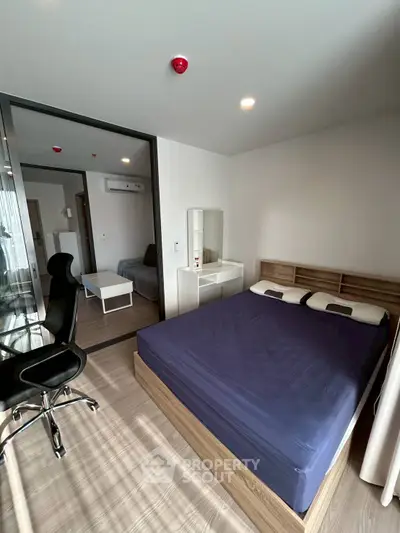 Modern bedroom with blue bedding and office chair, featuring a sleek design and natural light.