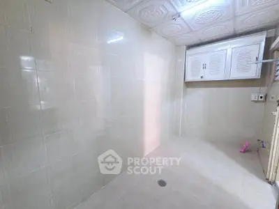 Spacious tiled utility room with ceiling storage cabinets and drain, ideal for laundry setup.