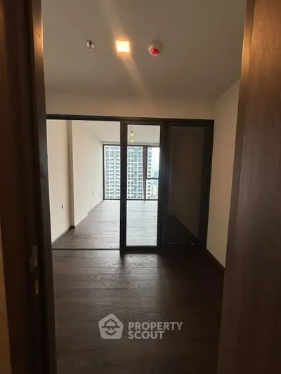 Spacious modern apartment with floor-to-ceiling windows and dark wood flooring, offering city views.