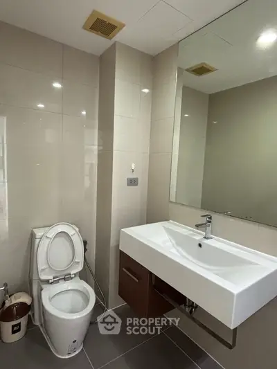 Modern bathroom with sleek fixtures and neutral tiles, featuring a spacious sink and toilet.