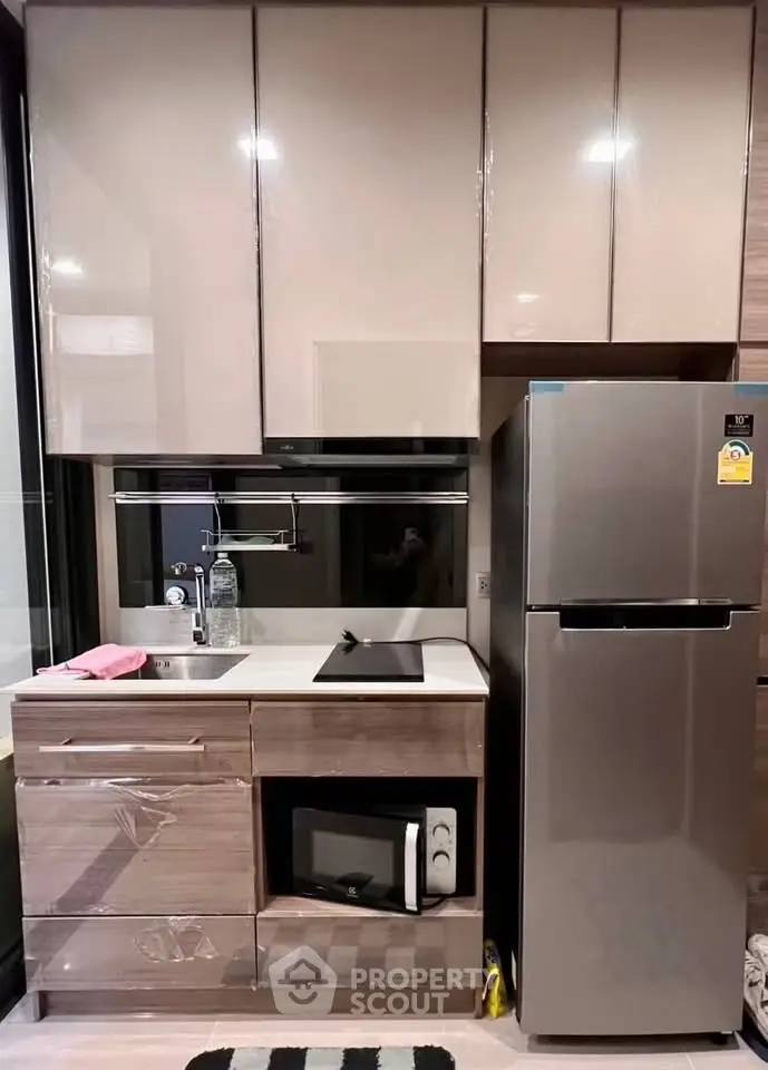 Modern compact kitchen with sleek cabinets, stainless steel fridge, and built-in microwave.