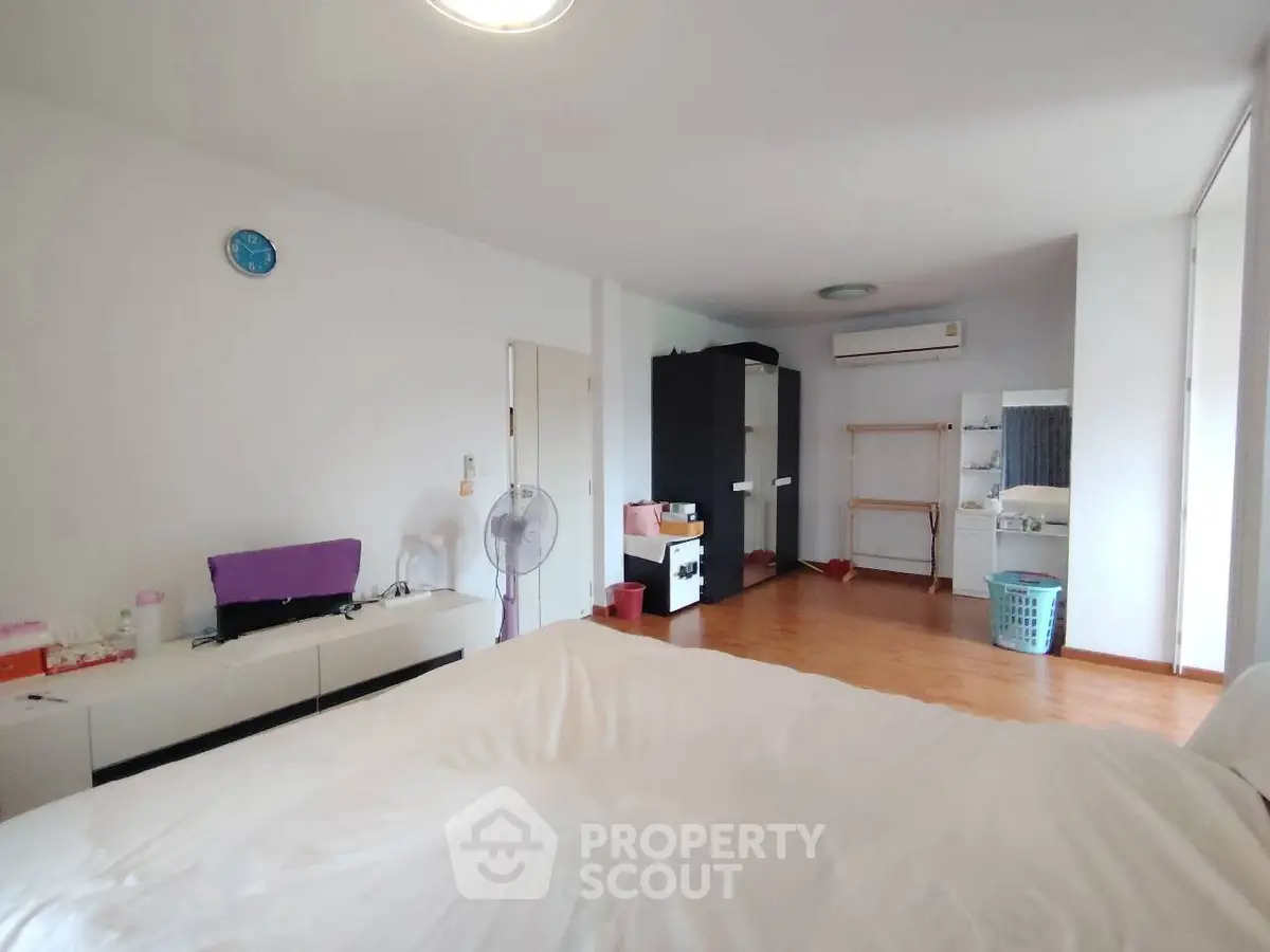 Spacious bedroom with modern decor and ample natural light, featuring wooden flooring and minimalist furniture.