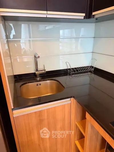 Modern kitchen with sleek black countertop and wooden cabinetry, featuring a stylish sink and dish rack.
