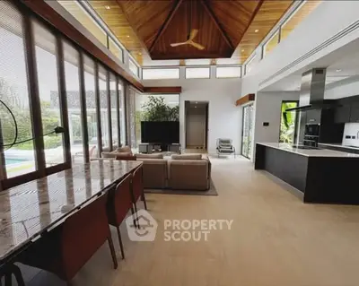 Luxurious open-plan living room with high ceilings and modern kitchen, featuring large windows and elegant decor.