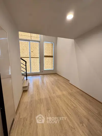 Spacious modern room with wooden flooring and large windows, perfect for a cozy living area.