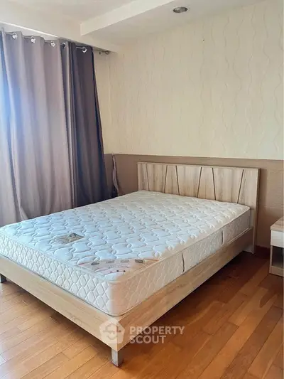 Spacious bedroom with wooden flooring and modern design, featuring a comfortable bed and elegant curtains.