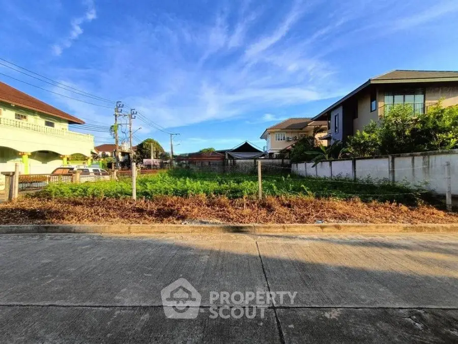 Vacant residential land plot in a suburban neighborhood with clear blue sky.
