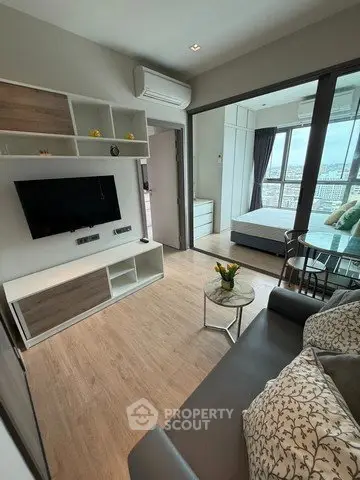 Modern living room with open view to bedroom, featuring sleek furniture and natural light.