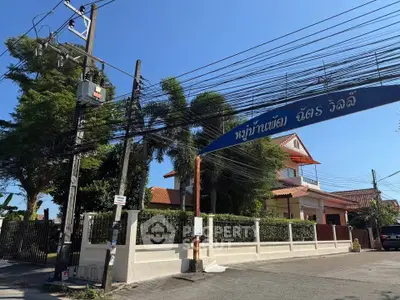Charming residential entrance with lush greenery and traditional architecture under clear blue skies.