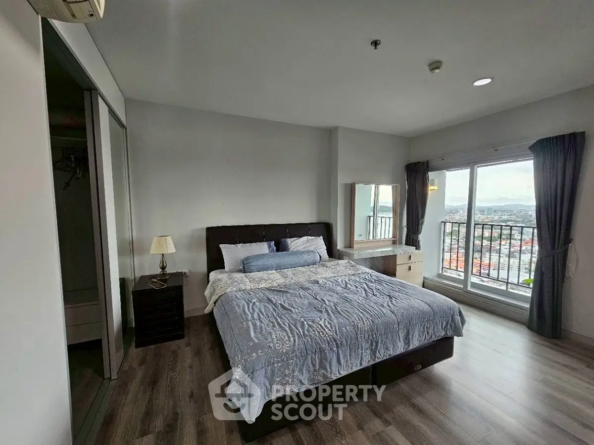 Spacious bedroom with large window and city view, featuring modern decor and wooden flooring.