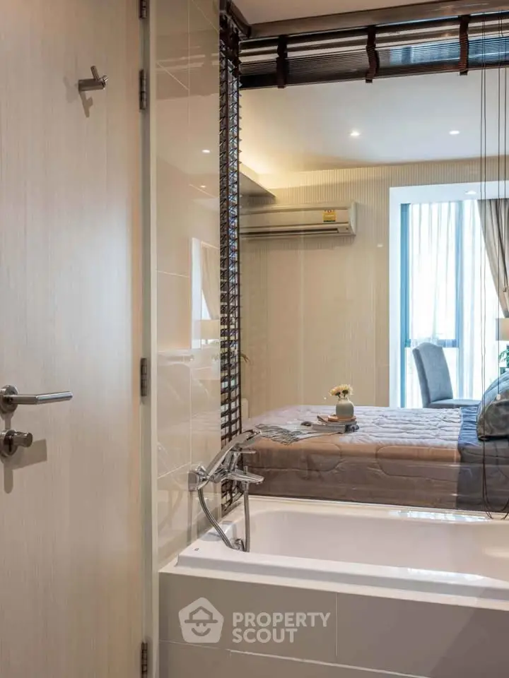 Modern bathroom with bathtub and view into a stylish bedroom, featuring sleek design and natural lighting.