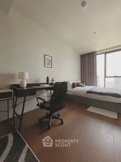 Modern bedroom with study area, featuring sleek desk and comfortable bed, offering city views through large window.