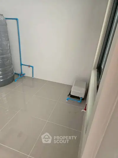 Spacious utility room with tiled flooring and plumbing setup, ideal for laundry or storage.