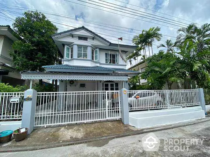 Charming two-story house with lush greenery and gated entrance in a serene neighborhood.