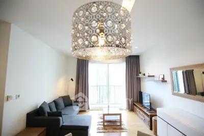 Modern living room with elegant chandelier, cozy sofa, and natural light from large window.