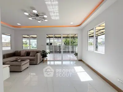 Spacious modern living room with large windows and elegant lighting, opening to a sunlit balcony.