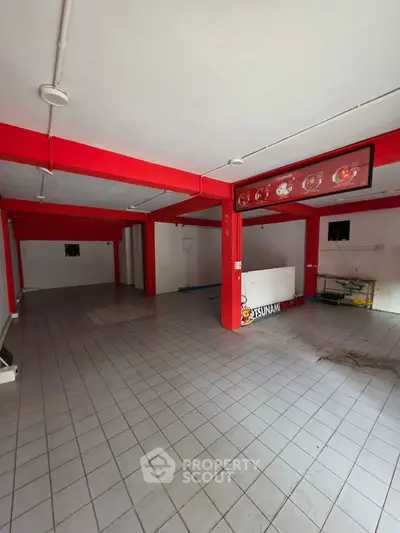 Spacious commercial property with vibrant red beams and tiled flooring, ideal for business setup.