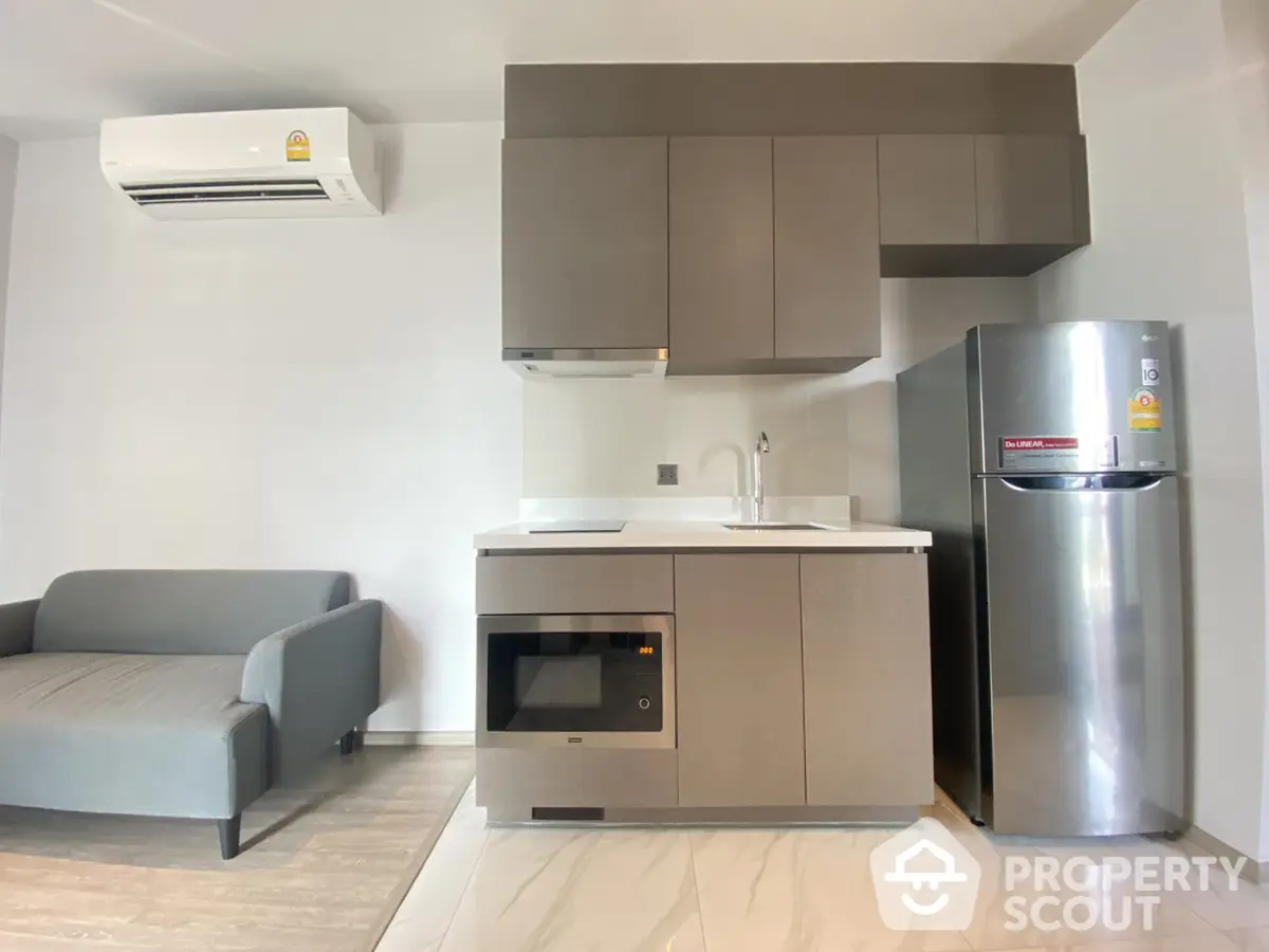 Modern studio apartment with integrated living space featuring sleek kitchen appliances, comfortable sofa, and air conditioning unit.