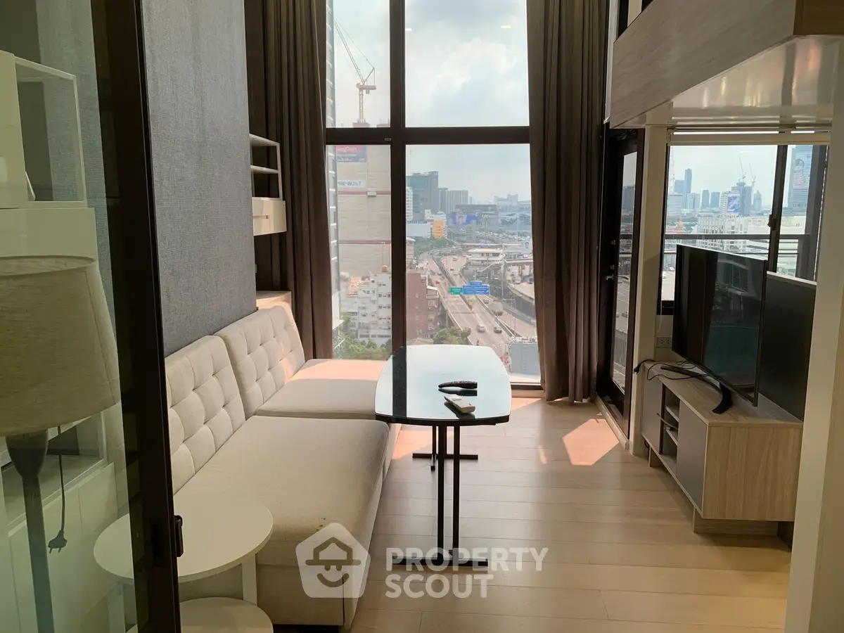 Modern living room with large windows offering stunning city views, featuring a cozy sofa and sleek TV setup.