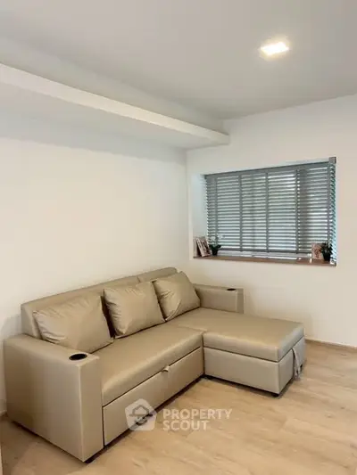 Modern living room with beige sectional sofa and large window with blinds.