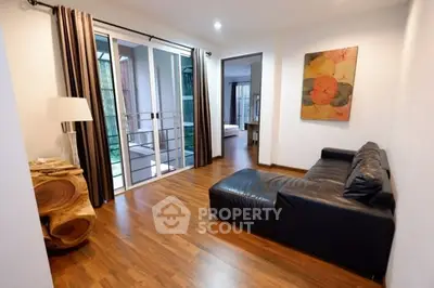 Modern living room with leather sofa and wooden flooring, featuring sliding glass doors to balcony.