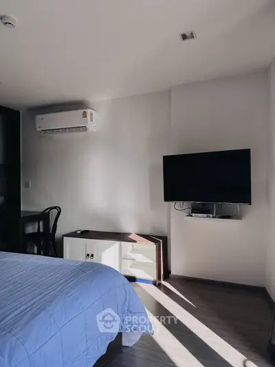 Modern bedroom with wall-mounted TV and air conditioning, featuring sleek furniture and natural light.