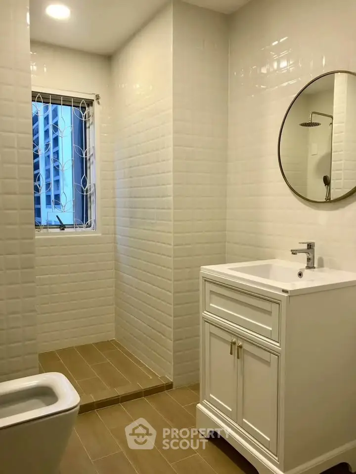 Modern bathroom with elegant white vanity and round mirror, featuring a sleek shower area and natural light.