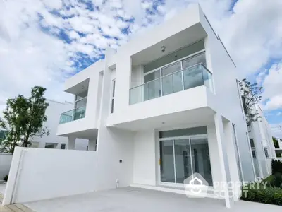 Modern white two-story house with large windows and balcony under a blue sky.