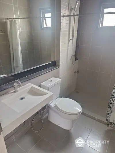 Modern bathroom with sleek fixtures and neutral tiles, featuring a shower and large mirror.