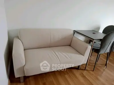 Cozy living room with modern beige sofa and sleek dining table on wooden flooring.
