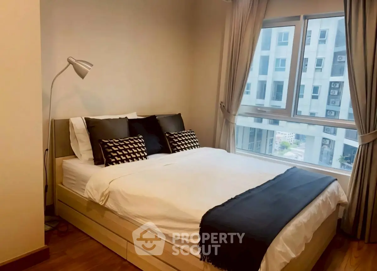 Cozy bedroom with modern decor and large window offering city view.