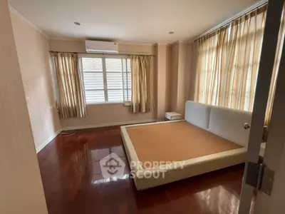 Spacious bedroom with wooden flooring and large windows for natural light