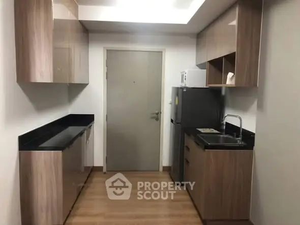 Modern kitchen with sleek cabinetry and compact design, featuring a refrigerator and built-in sink.