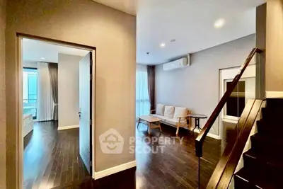 Modern duplex apartment with sleek wooden flooring and cozy living area, featuring a stylish staircase and ample natural light.