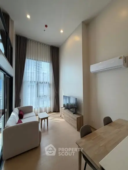 Modern living room with high ceilings and large windows, featuring a cozy sofa and sleek TV setup.