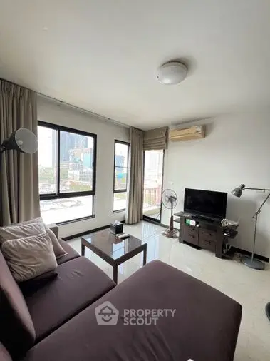 Spacious and well-lit living room with large windows offering an urban view, complemented by modern furnishings and a cozy ambiance.